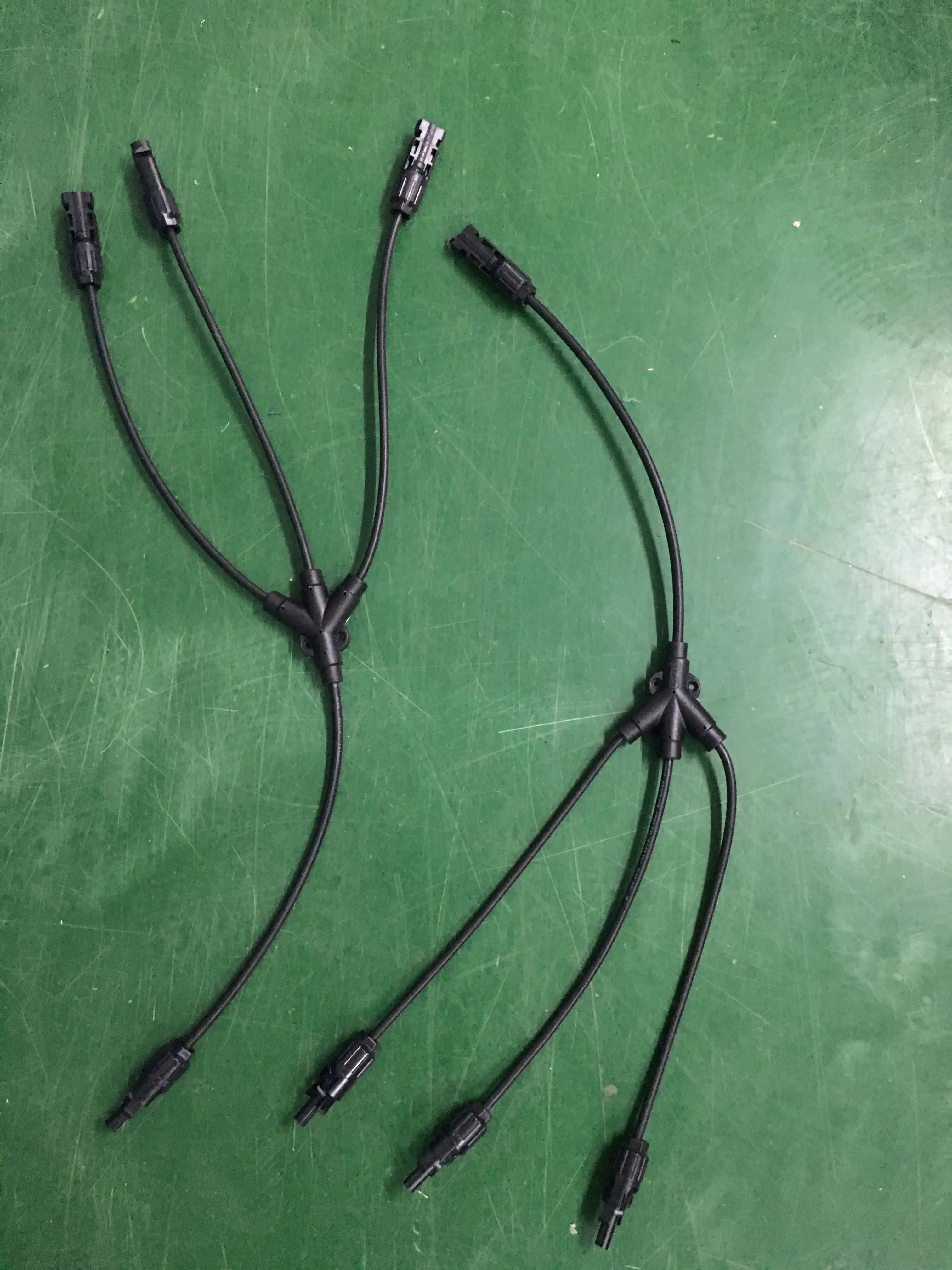 Two PVconnectorpro CM31-B 1000V DC solar PV Y-branch connectors on a green work surface, showcasing waterproof T-type 3-in-1 connectors.